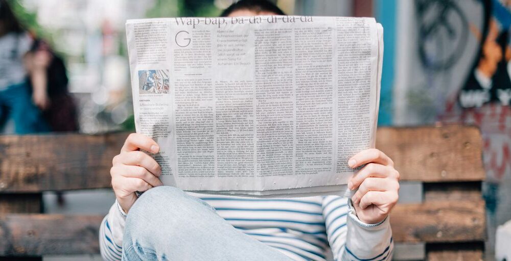 man sitting on bench reading newspaper