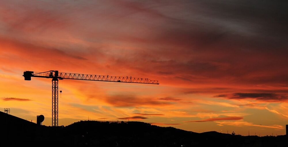 silhouette of crane and hill under cloudy sky photo taken during sunset