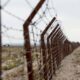 Empty US-Mexico border with barbed wire and vehicles.