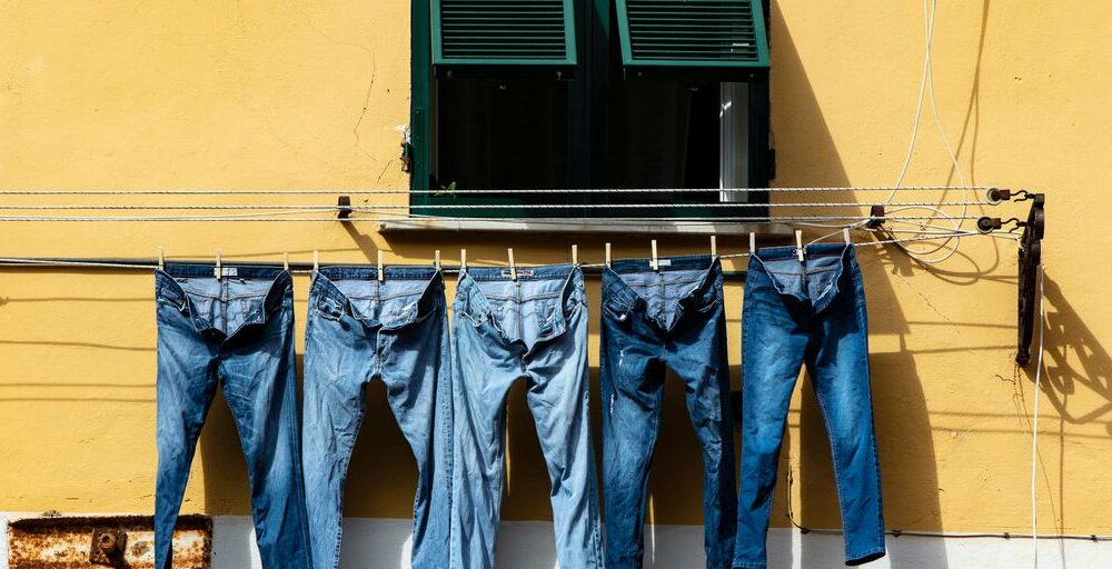 five blue denim jeans hanged on grey cable near window