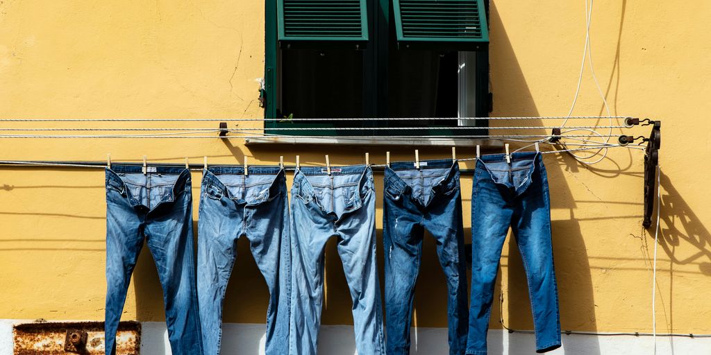 five blue denim jeans hanged on grey cable near window