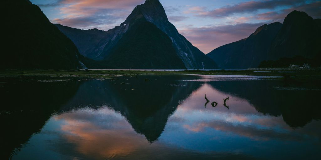 photo of lake with reflection of mountains under cloudy sky