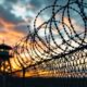 Border wall with barbed wire under a dramatic sky.