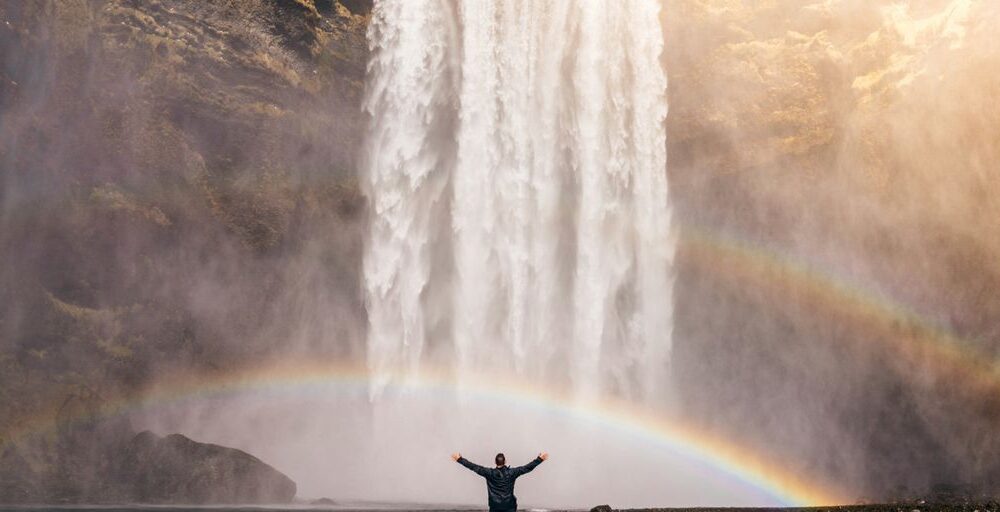 person in front of waterfalls with double rainbow during daytime