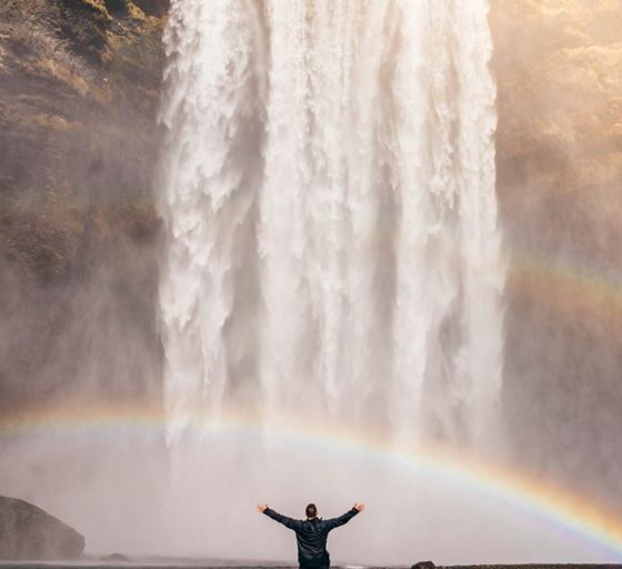 person in front of waterfalls with double rainbow during daytime