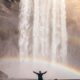 person in front of waterfalls with double rainbow during daytime