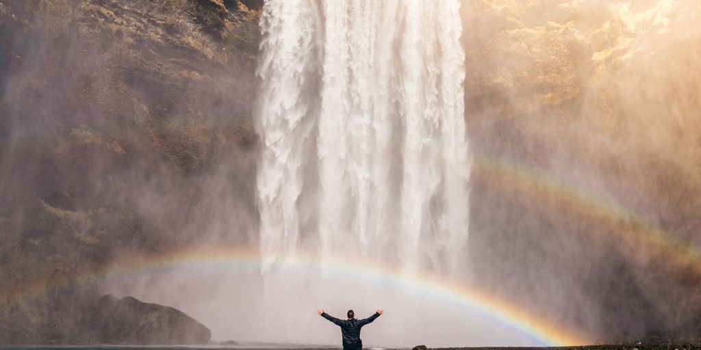 person in front of waterfalls with double rainbow during daytime