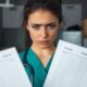 Healthcare worker with empty data sheets in dim office.