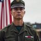 Military member in uniform with American flag backdrop.