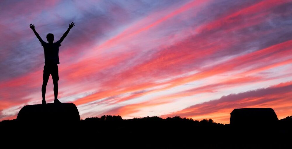 silhouette of man standing on high ground under red and blue skies