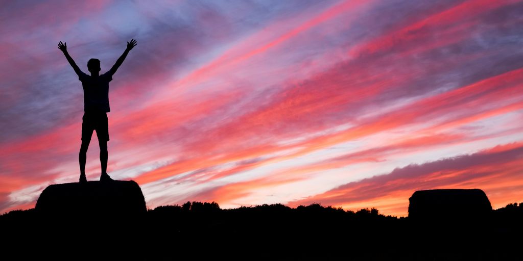 silhouette of man standing on high ground under red and blue skies