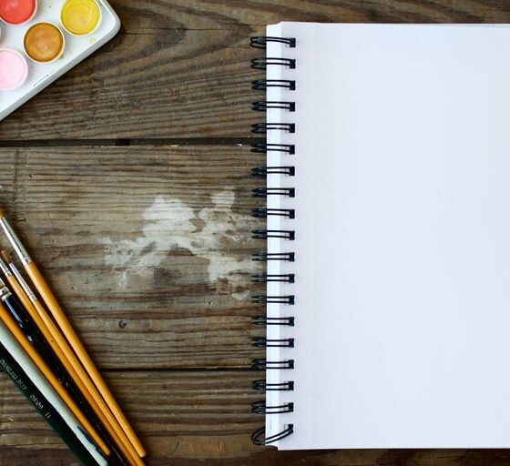 paint brushes next to drawing book and water color palette