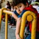 boy in blue and red shirt holding yellow metal bar