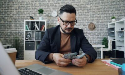 a man sitting at a table with a laptop and money