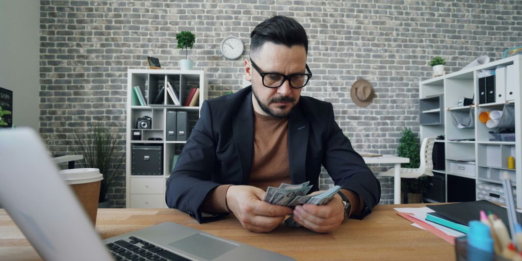 a man sitting at a table with a laptop and money