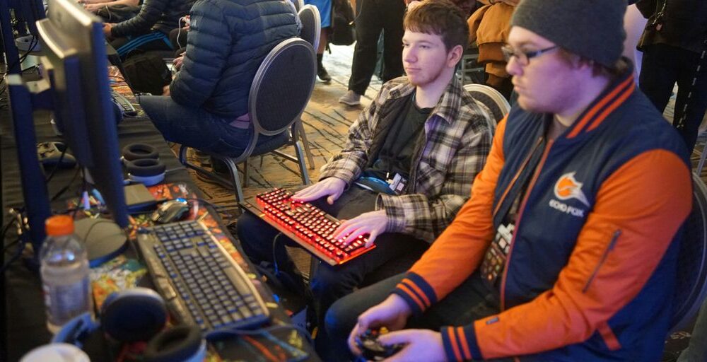 man using video game control pad beside man using computer keyboard sitting and playing video games