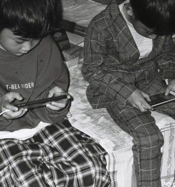 two young boys sitting on a bed looking at their cell phones