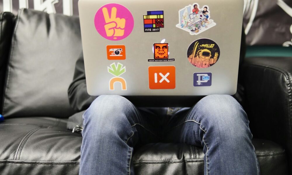 man using silver MacBook sitting on black leather sofa