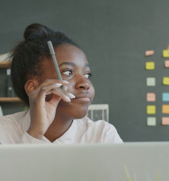 Young woman holding pencil, thinking at desk.
